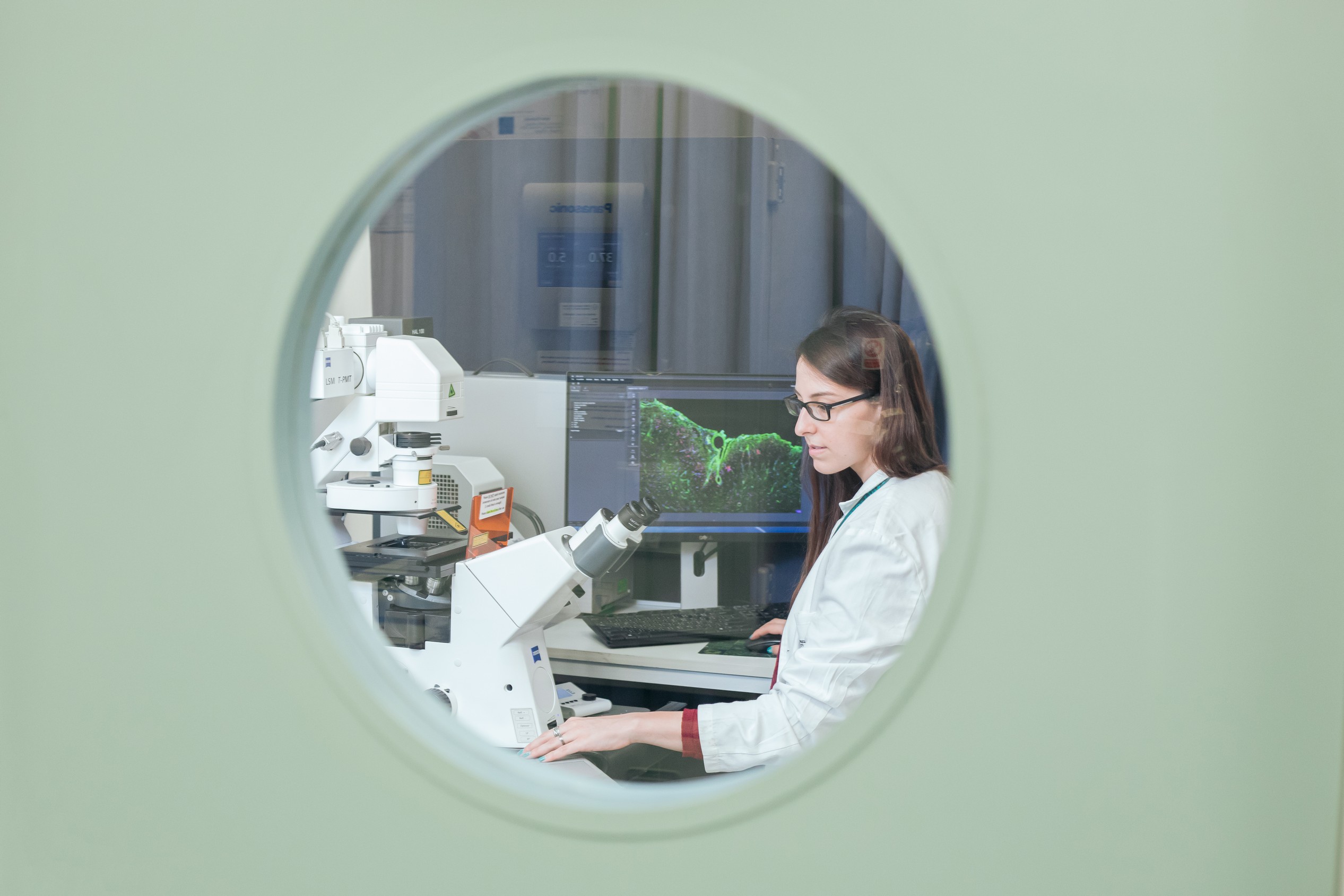 A researcher working in a lab, seen through the glass window of the door.